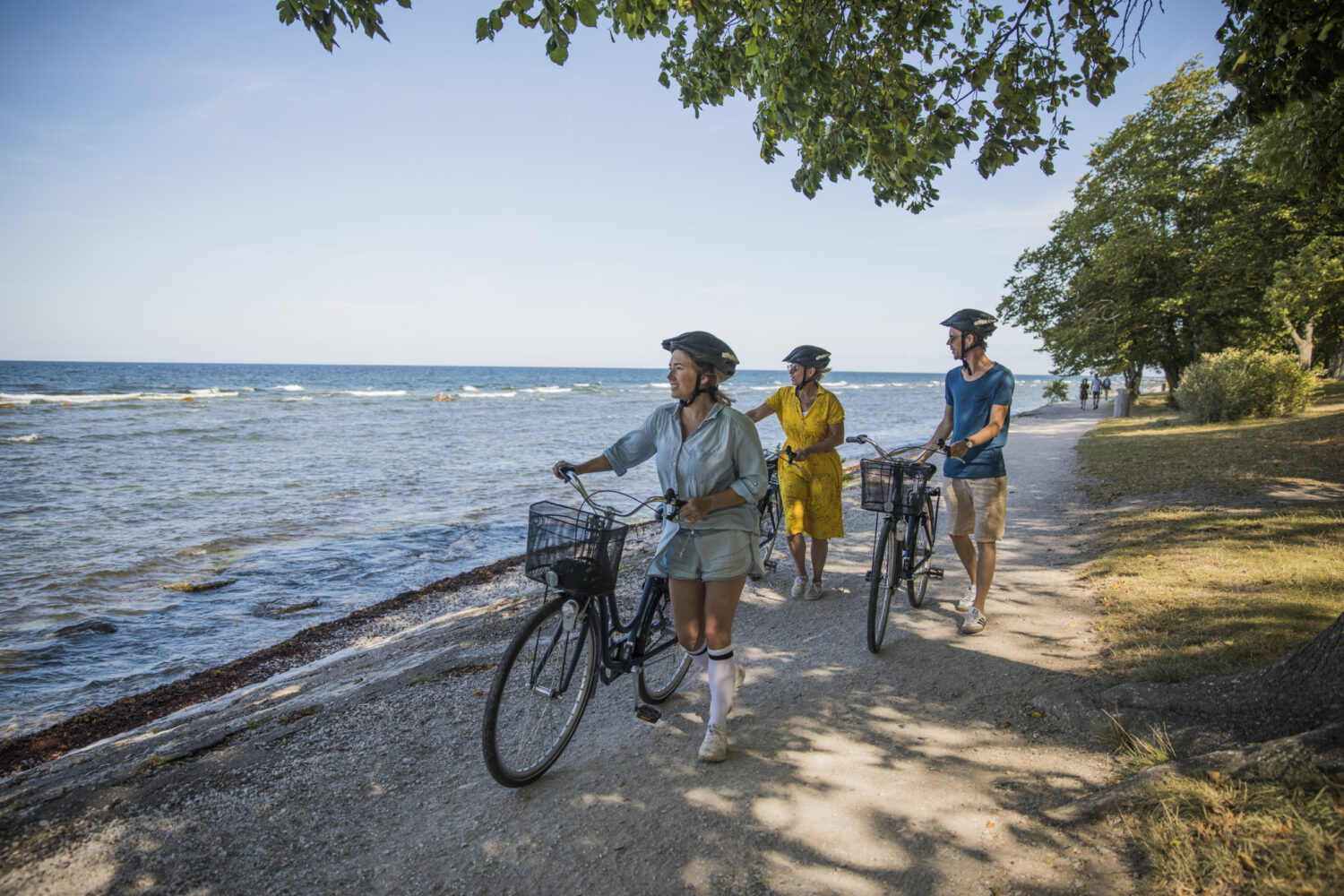 Tre personer leder sina cyklar längs strandpromenaden i Visby