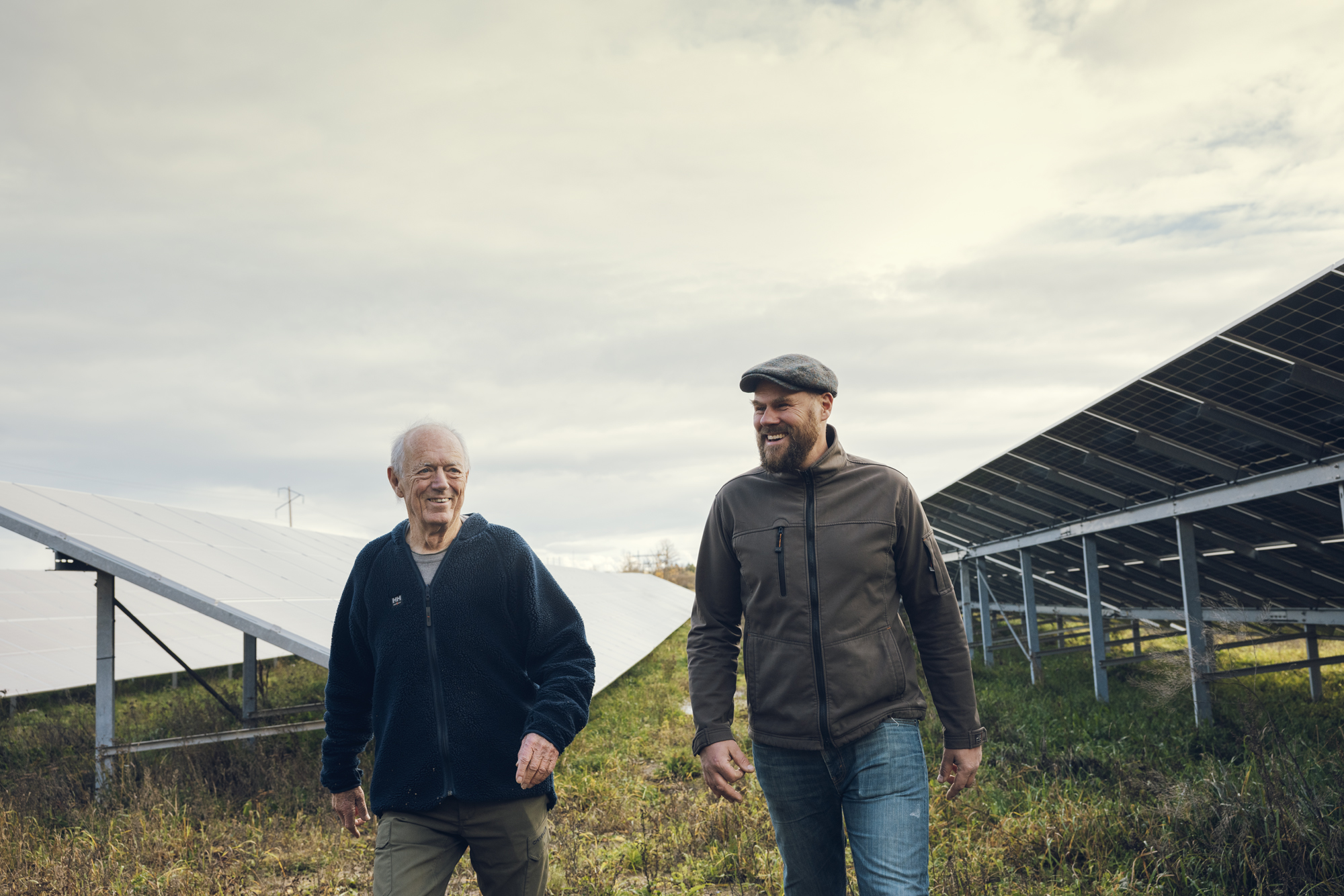 Två män vandrar mot kameran och i bakgrunden syns en solcellspark