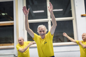 Tre äldre herrar i gula träningströjor på gymnastik